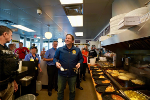 DeSantis stands in front of a Waffle House grill in front of food it appears he served out.