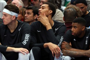 Spurs center Victor Wembanyama, center, sits on the bench during the team's NBA basketball game against the Dallas Mavericks on Saturday, 