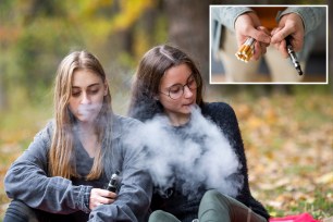 Teenage girls in casual clothes vape electronic cigarette on the street in the park in the autumn evening