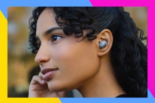 A woman with curly hair wearing wireless earbuds.