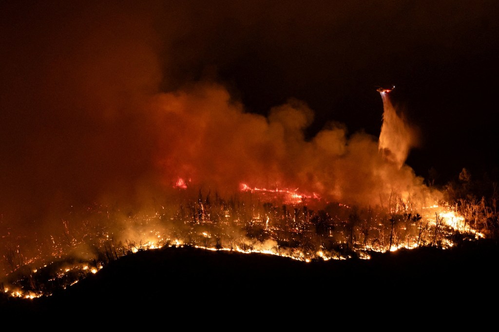 A helicopter drops water over the Thompson wildfire as firefighters continue battling fire into the night near Oroville, California