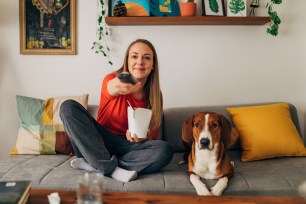 Young woman enjoying a TV marathon on her sofa with her dog and a bowl of takeout pasta