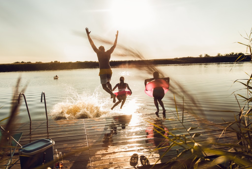 Friends having fun enjoying a summer day swimming and jumping at the lake.