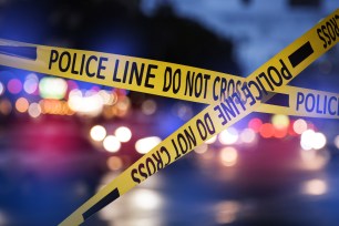 Yellow police line tape isolating a blurred crime scene on a city street lit by red and blue police car lights after a shooting incident