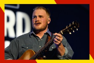 Zach Bryan eyes his crowd from the stage while strumming a guitar.