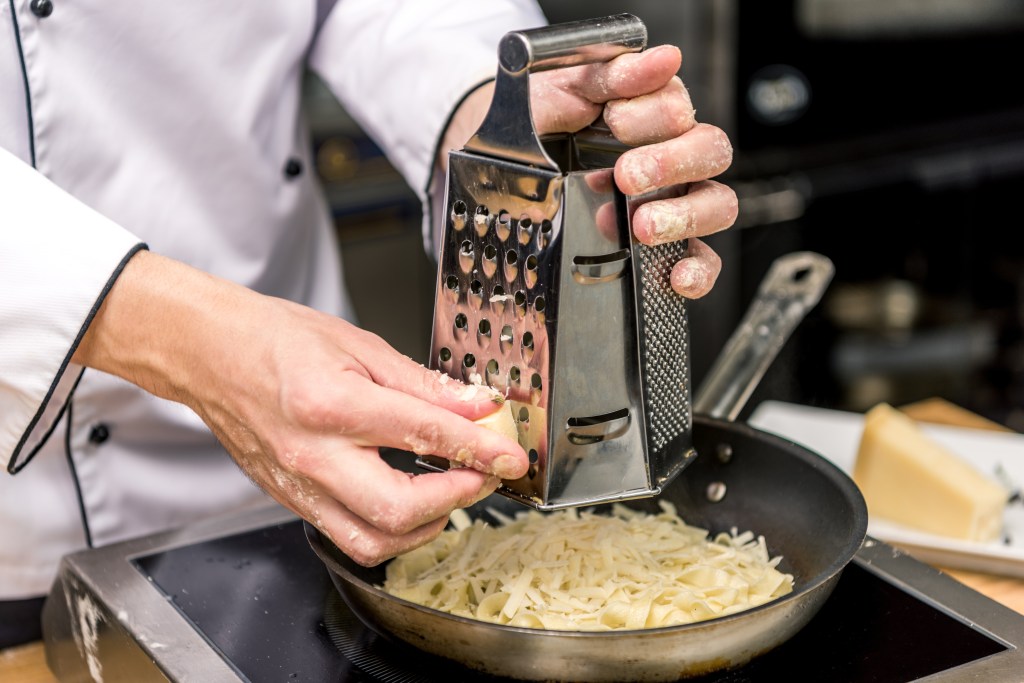 Cropped image of a chef grating cheese on a grater, creating perfect slices