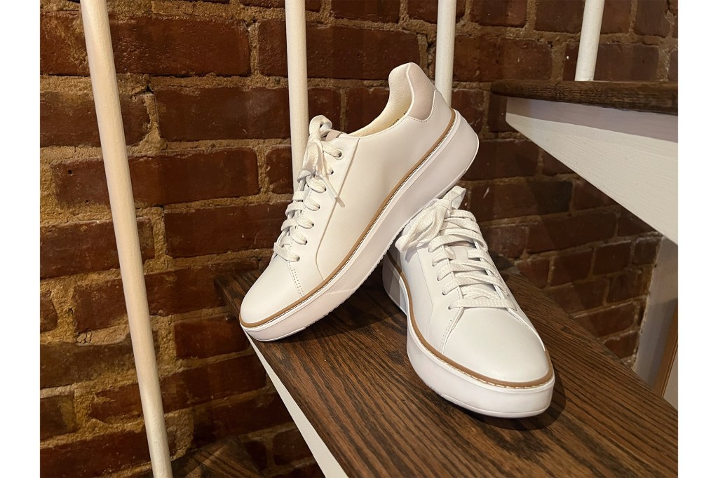 A pair of white Cole Haan shoes on a wooden shelf.