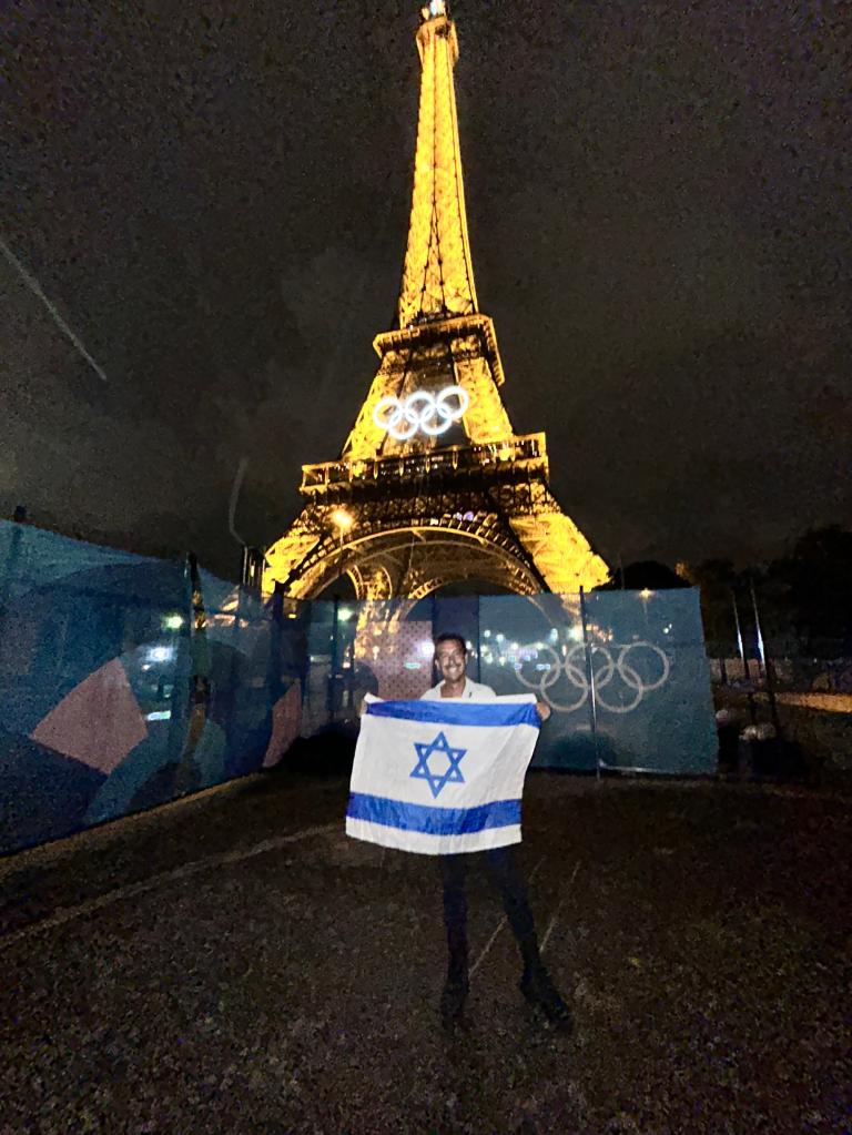 Neil Frias standing with an Israeli flag in front of the Eiffel Tower. 