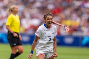 A woman in a white uniform with a pink braid in her hair celebrating a soccer win