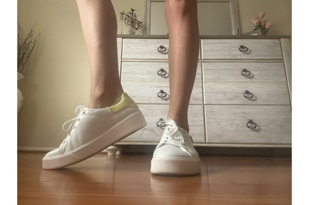 A person's legs and feet wearing white shoes