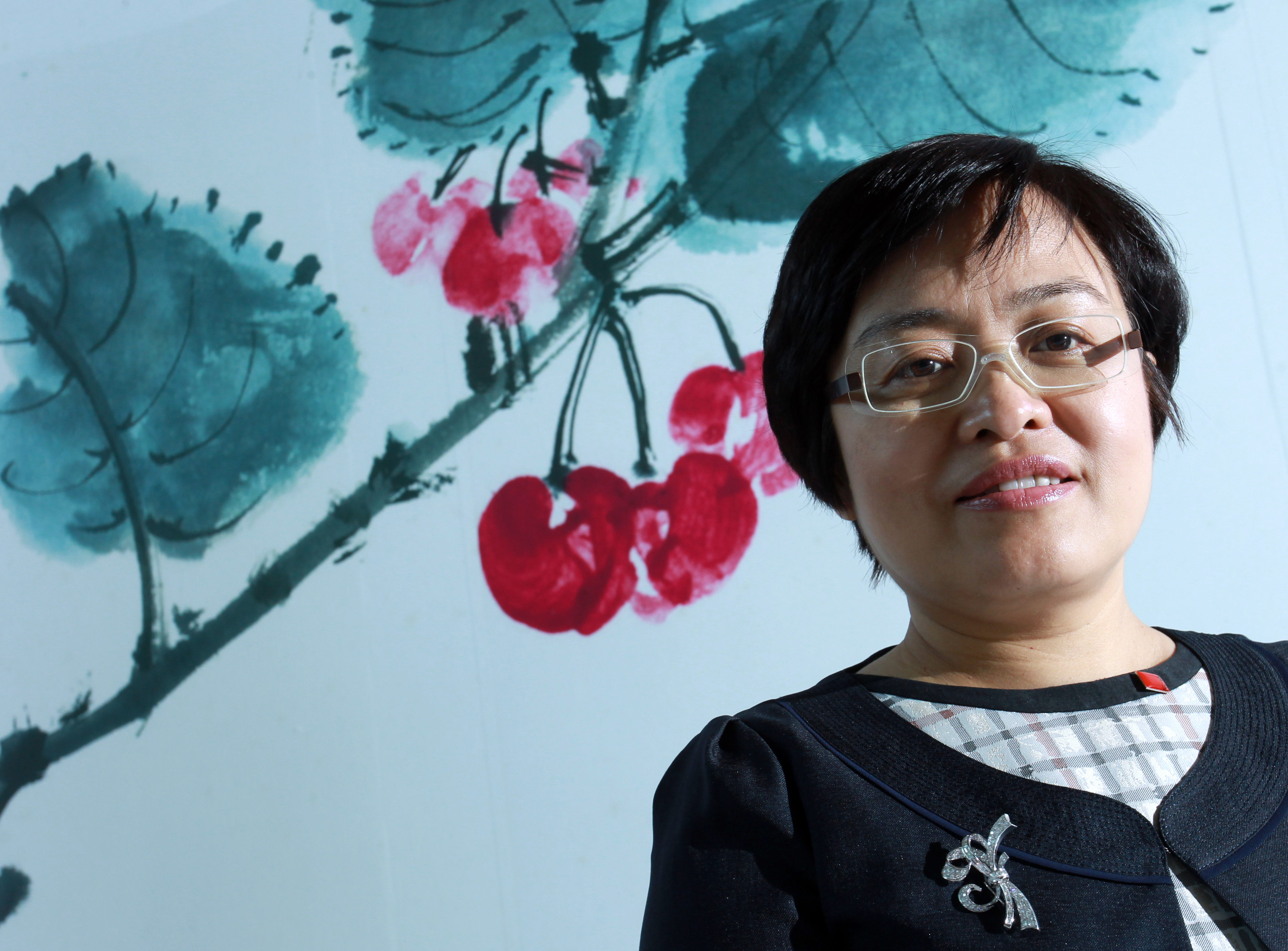 Middle aged Asian woman with short hair poses in front of drawing of cherries