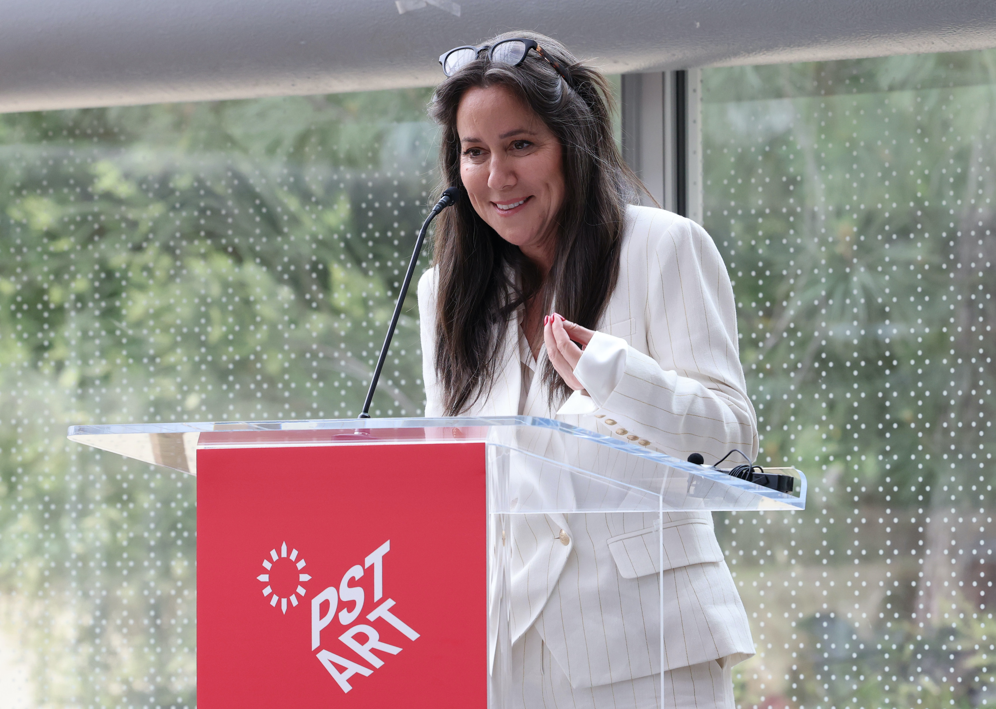 Woman with brown hair dressed in white suit speaks at red podium.