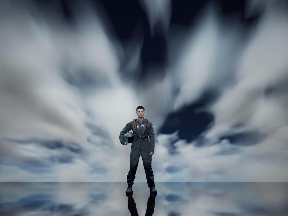 A woman in pilot gear stands in front of a backdrop of clouds