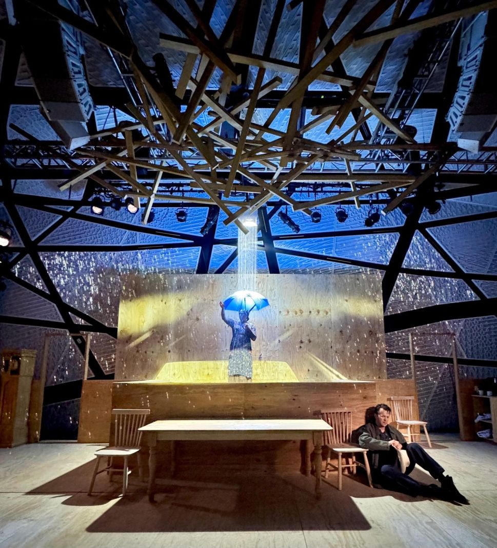 Rain pours onto a performer holding an umbrella on a well-lit stage