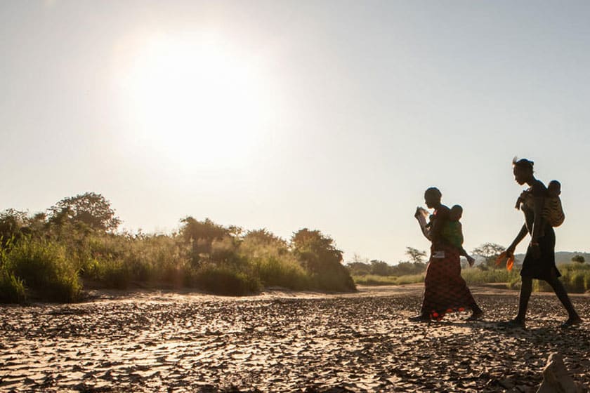 two people walk across a dry field of cracked mud. UNICEF/UNI308044/Schermbrucker