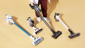 Four cordless vacuums on a brown background with legs of one person who is vacuuming