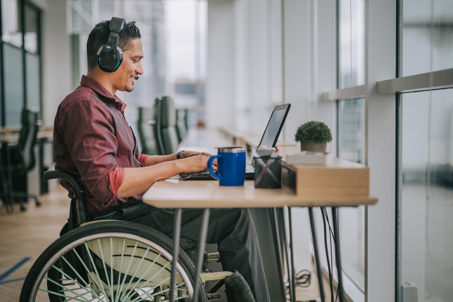 A man with a goatee wearing headphones and using a laptop computer, using a wheelchair at a table.