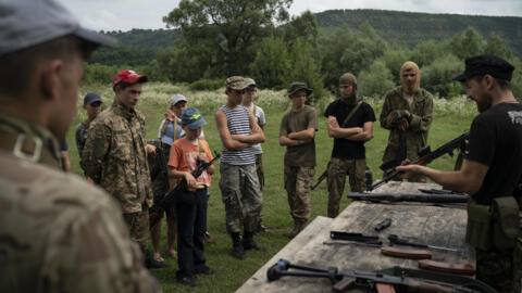 Yuri Chornota Cherkashin, right, head of Sokil, gives instructions on how to assemble an AK-47 rifle to young participants of the "Temper of Will" summer camp.