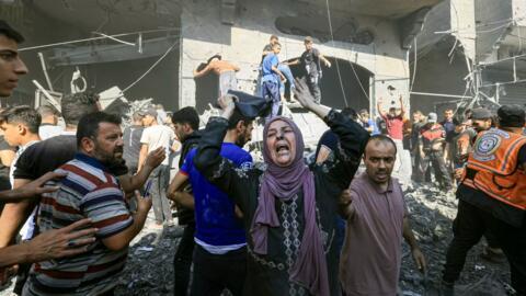 A Palestinian woman reacts as others rush to look for victims in the rubble of a building following an Israeli strike in Khan Younis in the southern Gaza Strip on 17 October 2023.