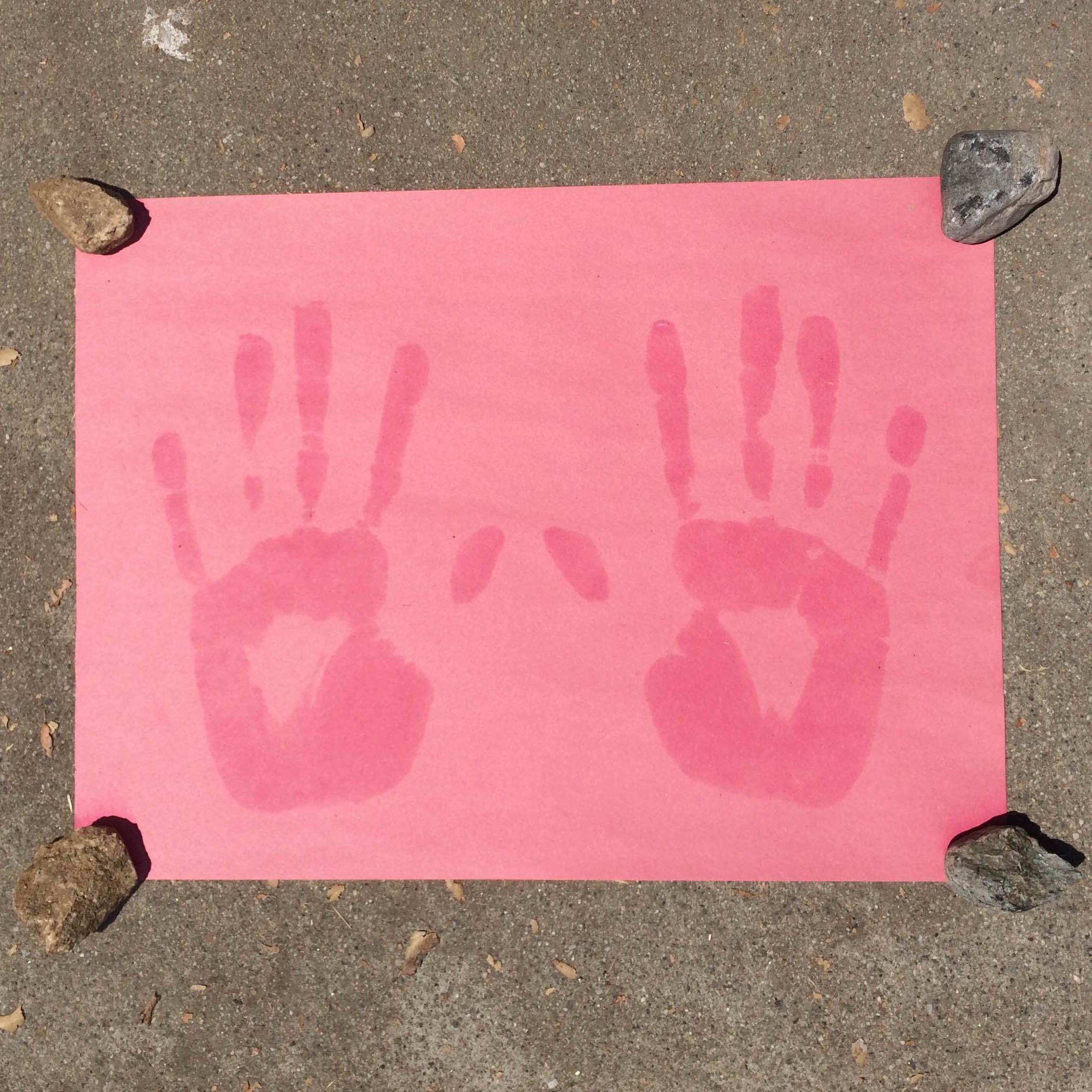 Image of a red piece of paper with two handprints on it that are darker red.