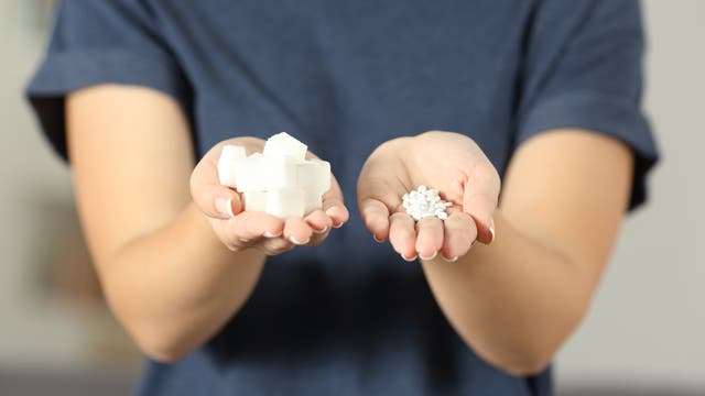 Eine Frau hält Zucker in der einen und Süßstoff in der anderen Hand