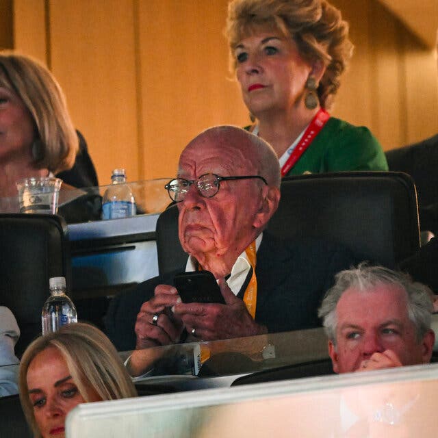 Rupert Murdoch is shown seated among several people, a cellphone in his hand.  