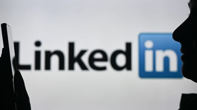 An image of a woman holding a cell phone in front of a LinkedIn logo displayed on a computer screen.