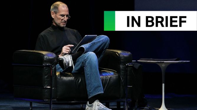 Steve Jobs on stage, sitting in a comfortable armchair and looking down at a first-generation iPad.