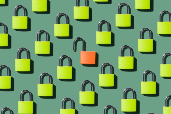 An Opened Orange Colored Lock Standing Out From Locked Green Colored Locks on Green Background Directly Above View.