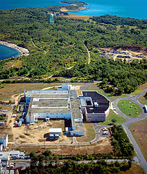 An aerial view of a compound, tree-filled terrain, and blue sea