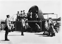 A large gun encased in an open backed metal turret atop a fort