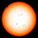 The sun in orange, as seen from the visible spectrum, with Venus in the top left quadrant