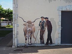 Photographie en couleurs d'une peinture sur un mur, représentant une vache et deux hommes.