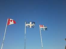 Drapeaux du Canada, du Québec et de Saint-Malo flottant au vent, par temps clair.
