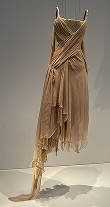 A mid-length ragged-looking dress hung from wires, with one longer piece of the hem dragging on the floor