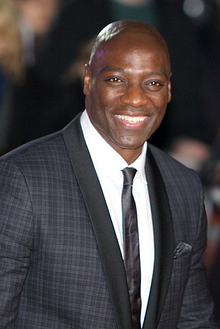 A black man, wearing a green shirt and a necklace of purple flowers.