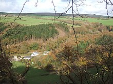 houses in wooded valley with green fields on the hill beyond