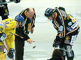 Photo de Oksanen qui jette un palet entre deux joueurs.