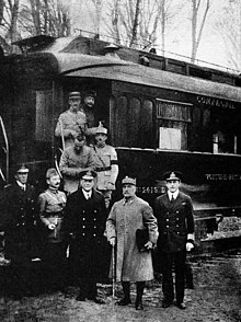 black and white photograph of five men in military uniforms standing side-to-m right, seen outside his railway carriage in the forest of Compiègne.