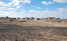 Photographie d'un paysage désertique, en arrière-plan duquel se trouve une ville.