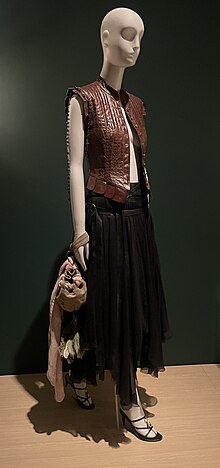 A sleeveless leather vest, black ankle-length skirt, heeled shoes, and a purse on a mannequin