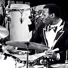 Elvin Jones in a black suit performing behind a drum kit