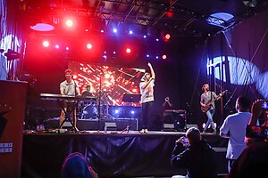 AJR performing "Bang!" in 2023. From left: Ryan playing an electronic keyboard, Jack singing, and Adam playing a bass guitar.