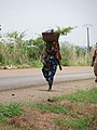 Femme marchant pieds nus, avec bébé au dos se rendant au marché sous un soleil ardent à Pobè au Bénin.