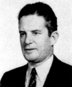 Grainy older portrait of a man wearing a suit and a tie. He is facing left, and has dark curly hair.