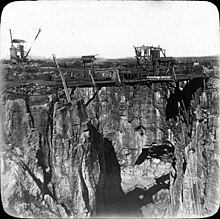 Photographie en noir et blanc d'une falaise d'une carrière à ciel ouvert, avec des échafaudages et des machines-outils sur le bord du trou.