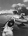 PhoM 1/c Joe Day (foreground) and PhoM 1/c Len Globus (top) examine a VB-10 SBD Dauntless, damaged during a photographic mission over Truk Atoll, 16-17 February 1944.