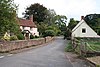 Street scene with houses and trees separated from the road by a stone wall.