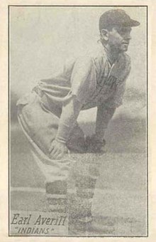 A man, wearing a baseball uniform stands with his hands on his knees.