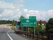 Green exit sign (in French and English) that has the New York State Route 9N symbol with the destinations listed as AuSable Forks and Keeseville.